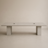 A minimalist rectangular concrete table with a thick top and two blocky legs, shown against a neutral beige studio background.